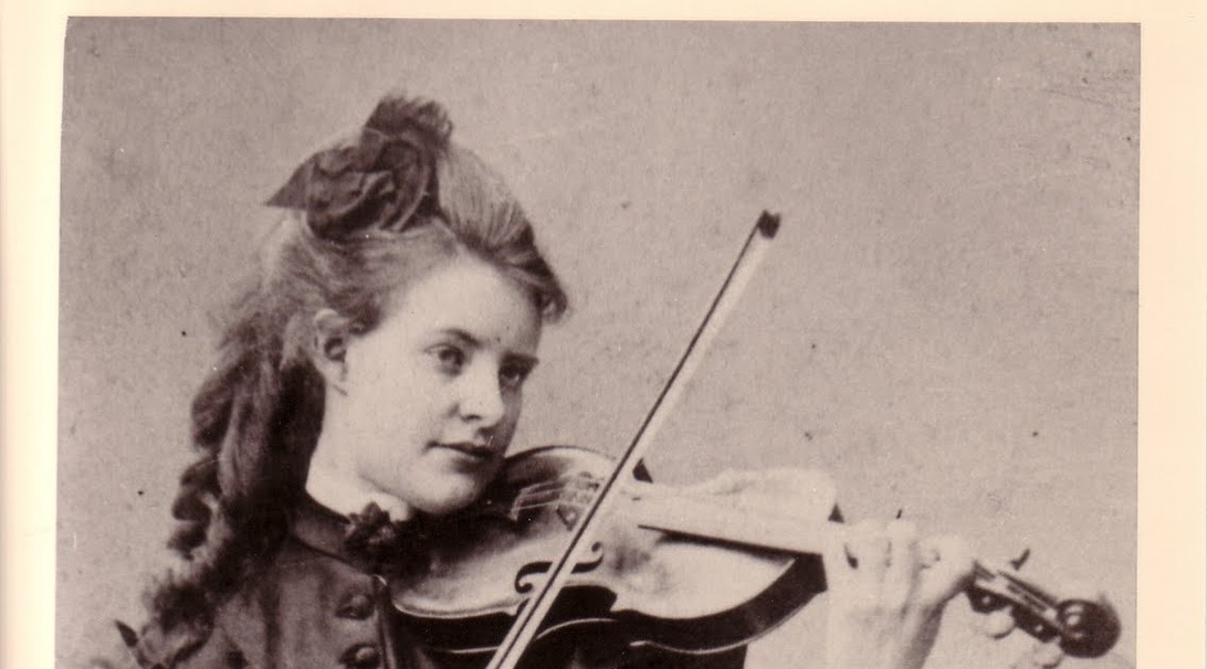 Historisk sort-hvidt fotografi af en ung kvinde med tidstypisk opsat hår, der spiller violin.
